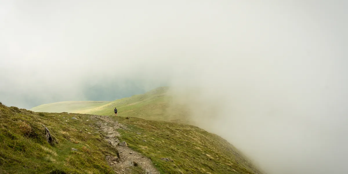 Cloud engulfing a lone hiker on the descent